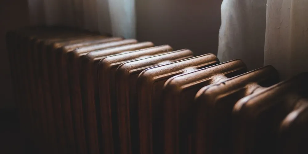 Radiateur ancien en fonte éclairé par une fenêtre voilée de rideaux