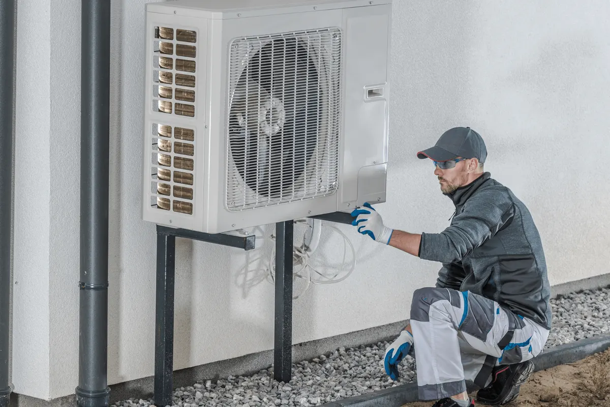 Technicien fixant le groupe extérieur d'une pompe à chaleur sur ses supports, au pied d'un mur